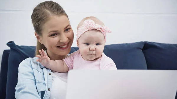 幸せな母親と赤ちゃんの女の子は前景にぼやけたノートパソコンを見て — ストック写真