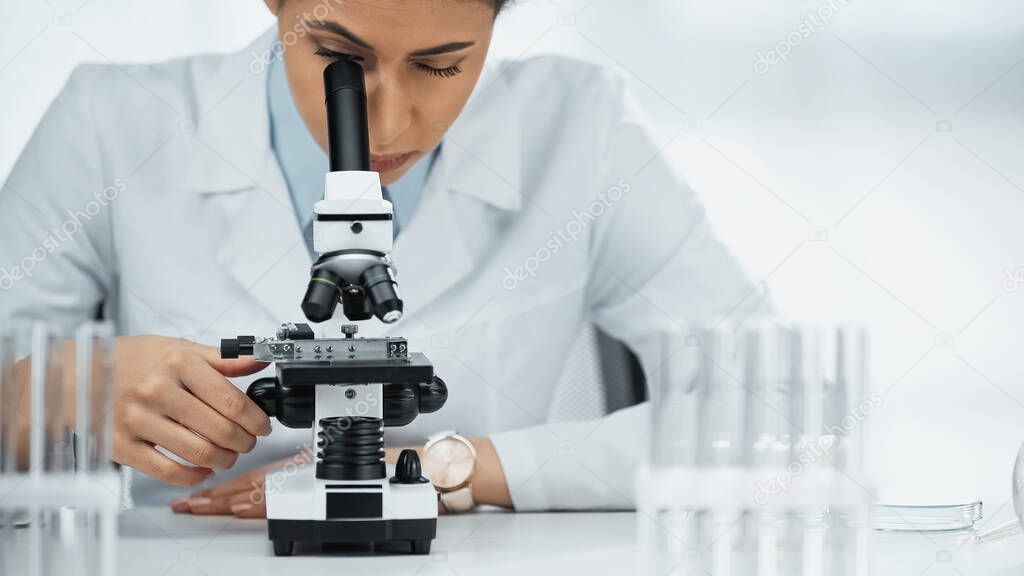 african american scientist in glasses looking through microscope in laboratory 