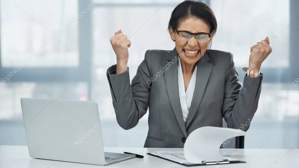 excited african american businesswoman in glasses near laptop