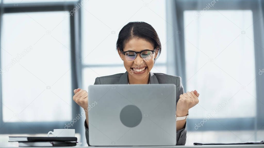excited african american businesswoman in glasses looking at laptop