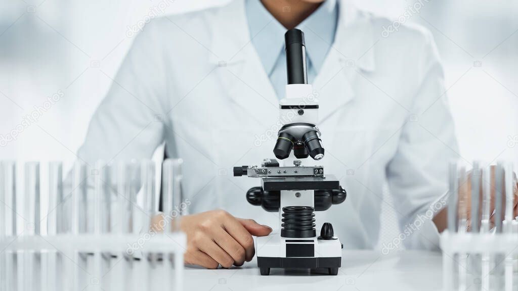 cropped view of african american scientist near microscope and test tubes in lab 
