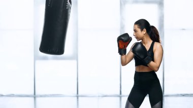 Spor salonunda kum torbasıyla çalışan odaklanmış bir kadının yan görüntüsü 