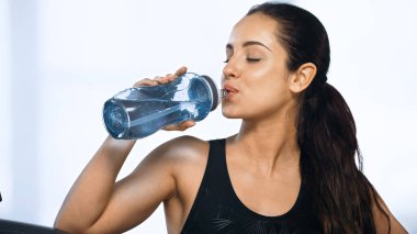 Spor şişesi tutan ve spor salonunda su içen genç bir kadın. 