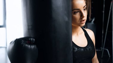 Boks eldivenli yorgun sporcu kadın kum torbasına yaslanıyor.