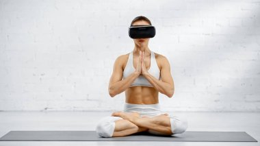 VR kulaklıklı genç kadın yoga pozunda oturuyor. 