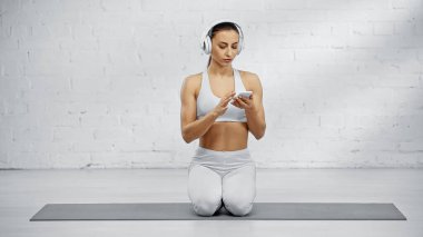Sporcu kadın kulaklıklı, fitness minderinde akıllı telefon kullanıyor. 