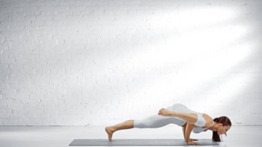 Beyaz duvarın yanında yoga yapan genç bir kadın. 