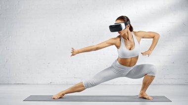 VR kulaklıklı çıplak ayaklı kadın yoga minderinin üzerinde duruyor. 