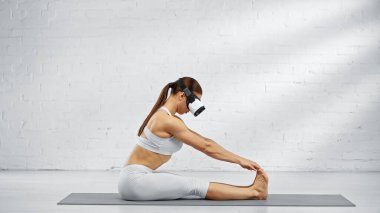 VR kulaklıklı bir kadının yoga minderinde öne eğilmesinin yan görüntüsü. 