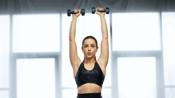 strong sportswoman in crop top exercising with dumbbells