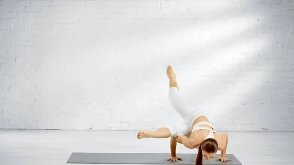 Young woman balancing on hands on yoga mat