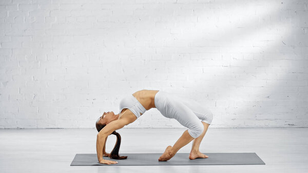 Side view of pretty woman bending back on yoga mat 