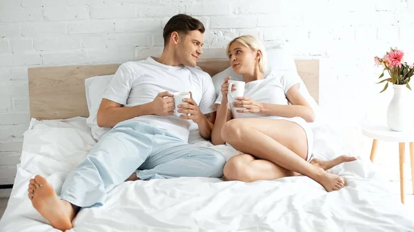 Young Couple Looking Each Other While Holding Cups Coffee Bed — Stock Photo, Image