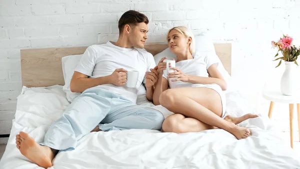 Young Couple Looking Each Other While Holding Cups Coffee Bed — Stock Photo, Image