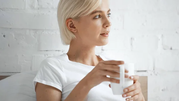 Beyaz Tişörtlü Sarışın Kadın Yatak Odasında Bir Fincan Kahve Tutuyor — Stok fotoğraf