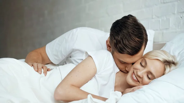 快乐的男人吻着笑着的女人 闭着眼躺在床上 — 图库照片