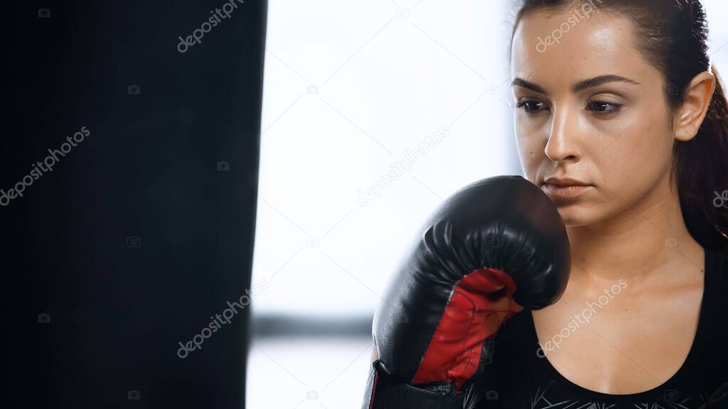 focused sportswoman in boxing glove training with punching bag in gym 