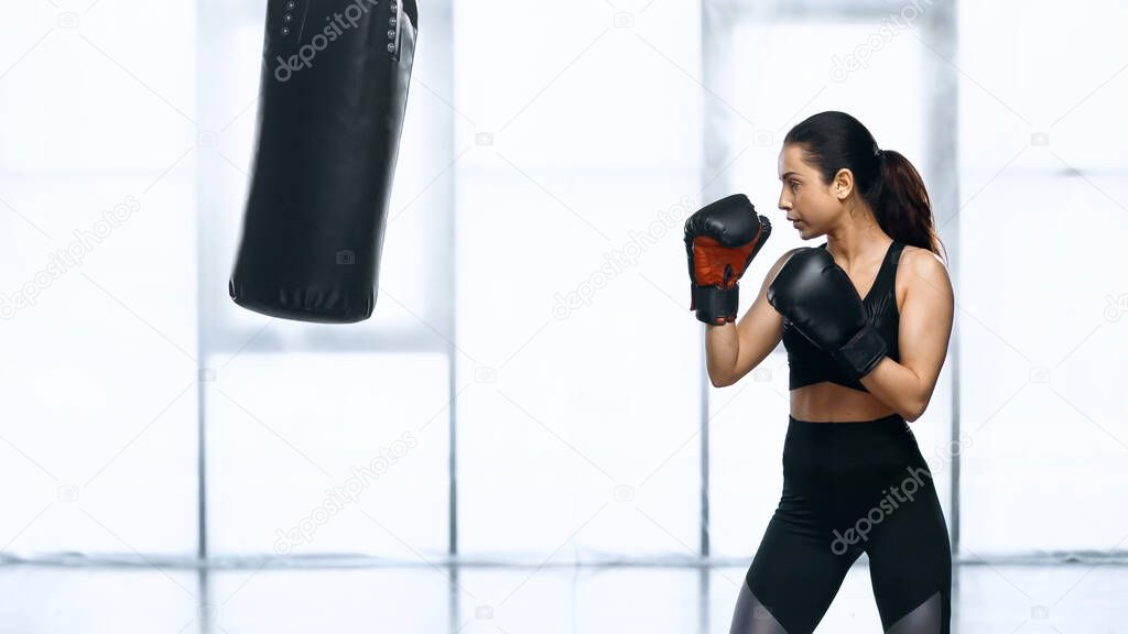 side view of focused woman training with punching bag in gym 