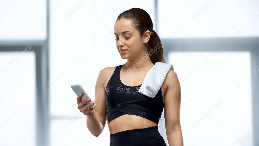 young sportswoman with towel looking at smartphone in gym 