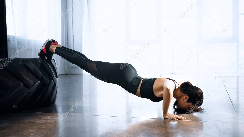 sportive young woman doing push ups near tire in sports center