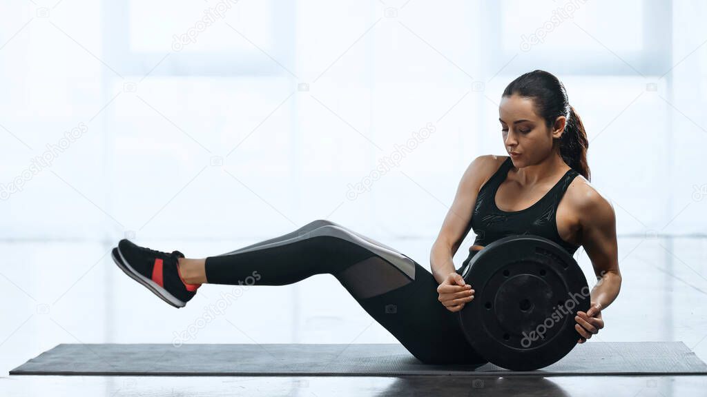 young sportswoman working out with weight plate on fitness mat in gym