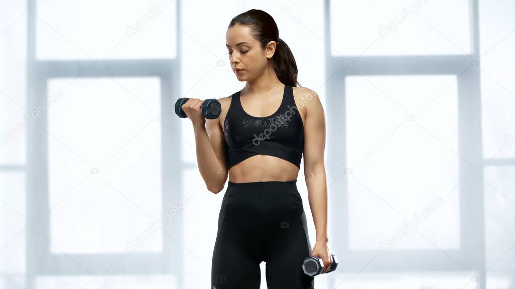 brunette sportswoman in crop top working out with dumbbells 