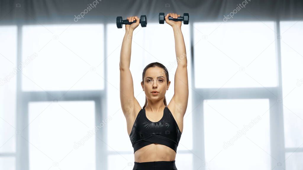 strong sportswoman in crop top exercising with dumbbells 
