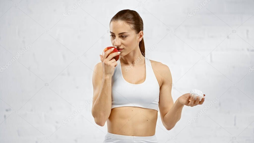 Fit sportswoman smelling apple and holding marshmallow