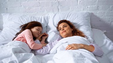 Yatakta uyuyan kızın yanında yatan bir kadın. 