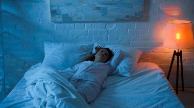 Pijamalı bir kadın geceleri beyaz yatakta uyuyor. 