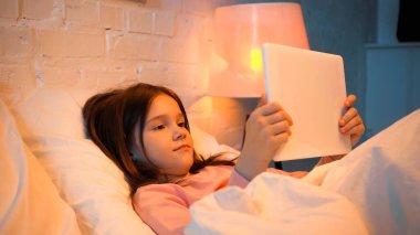 Çocuk yatakta dijital tablet kullanıyor. 