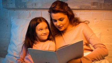 Akşamları elinde kitapla annesine bakan pozitif çocuk. 