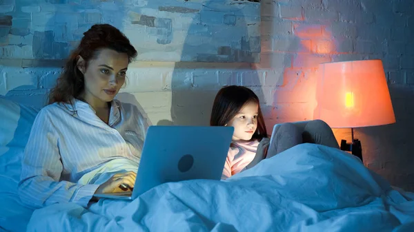 Vrouw Met Laptop Buurt Dochter Met Digitale Tablet Bed Nacht — Stockfoto