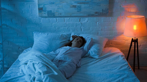 Woman in pajama sleeping on white bedding at night 