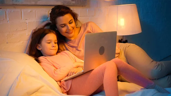 Criança Com Laptop Deitado Perto Mãe Positiva Cama — Fotografia de Stock