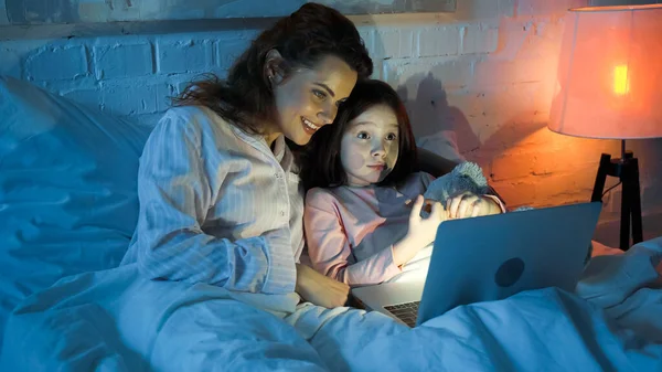 Donna Sorridente Pigiama Guardando Computer Portatile Vicino Bambino Con Peluche — Foto Stock