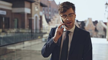 Modern alışveriş merkezinde gözlüklü mutlu iş adamı akıllı telefondan konuşuyor.