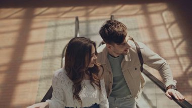 Alışveriş merkezinde yürüyen merdivende neşeli erkek ve kadının yüksek açılı görüntüsü 