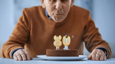 cheerful elderly man blowing out candles on birthday cake on grey background clipart