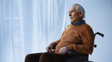 Tekerlekli sandalyedeki rüya gibi yaşlı adam huzur evinde oturuyor.