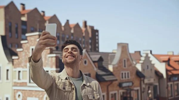 Fröhlicher Mann Macht Selfie Mit Verschwommenen Gebäuden Hintergrund — Stockfoto