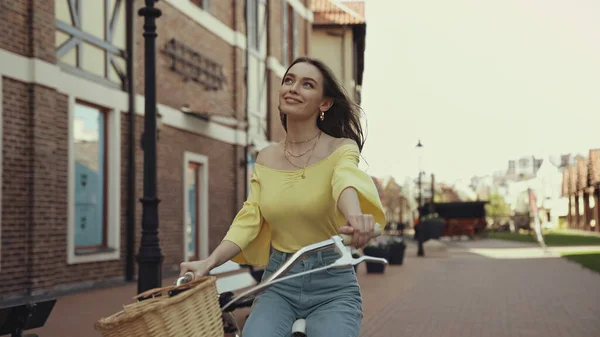 Ονειρεμένη Νεαρή Γυναίκα Κίτρινη Μπλούζα Χαμογελώντας Ενώ Ιππεύει Ποδήλατο Έξω — Φωτογραφία Αρχείου