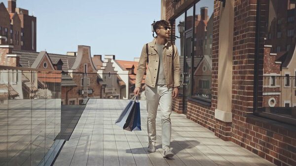 cheerful man in sunglasses holding shopping bags and walking outside