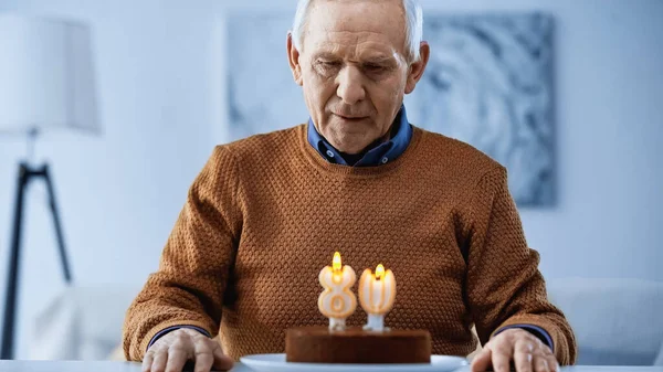 孤独的老人在客厅里看着生日蛋糕上燃着蜡烛 — 图库照片