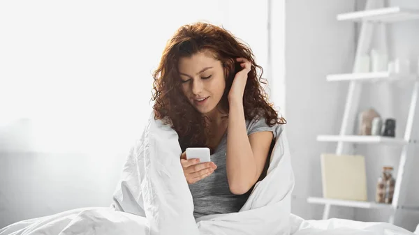 Curly Young Woman Wrapped White Blanket Using Smartphone Bedroom — Stock Photo, Image