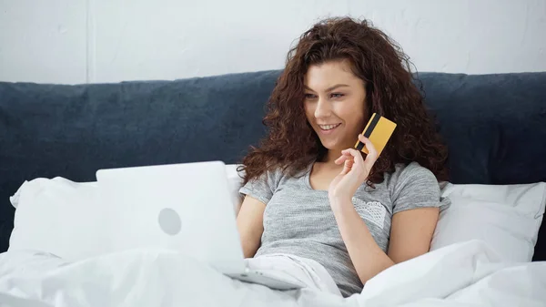 happy young woman holding credit card and using laptop while shopping online