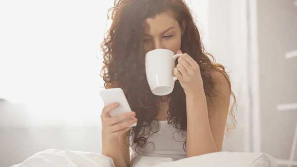 Young Curly Woman Drinking Coffee Using Smartphone — Stock Photo, Image