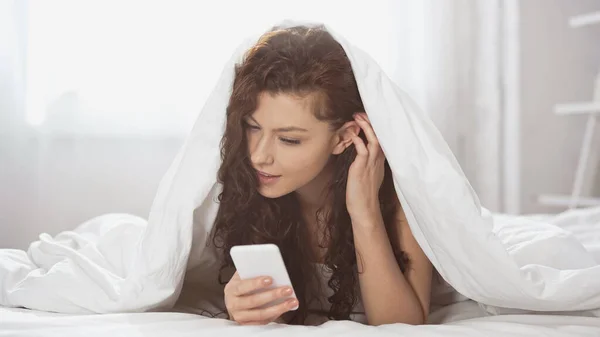 Mujer Joven Rizada Usando Teléfono Inteligente Mientras Está Acostado Debajo — Foto de Stock