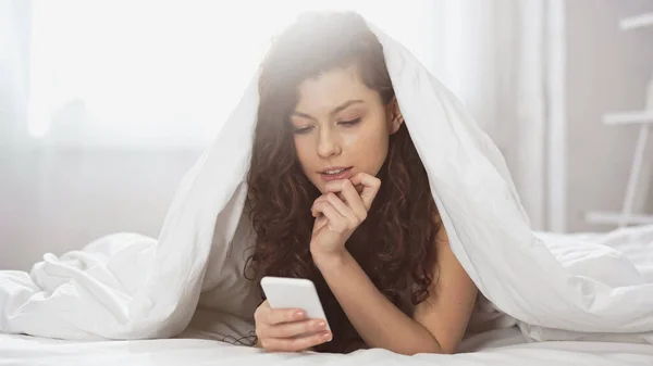 Giovane Donna Premurosa Utilizzando Smartphone Mentre Sdraiato Sotto Coperta — Foto Stock