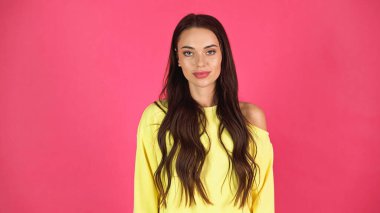 young adult woman in yellow blouse looking at camera isolated on pink